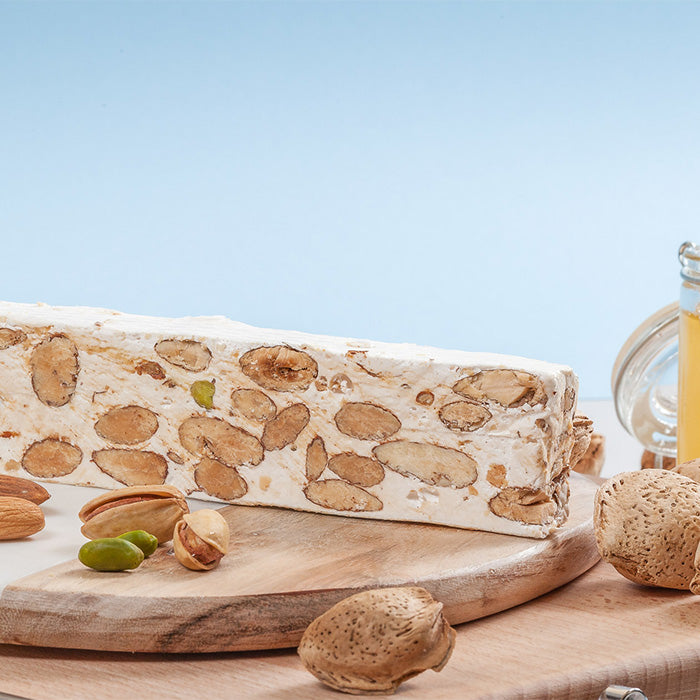 Barre de nougat de Provence entière posée debout avec amandes sur planche marbre et bois, fond bleu et couteau à bout rond