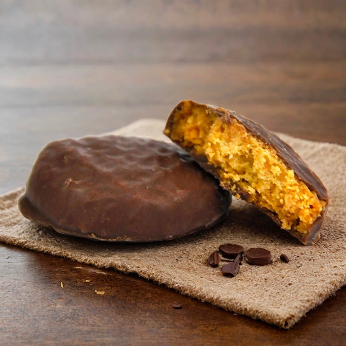 Sablé enrobé de chocolat au lait : un entier et un coupé révélant l'intérieur, posés sur serviette et table en bois