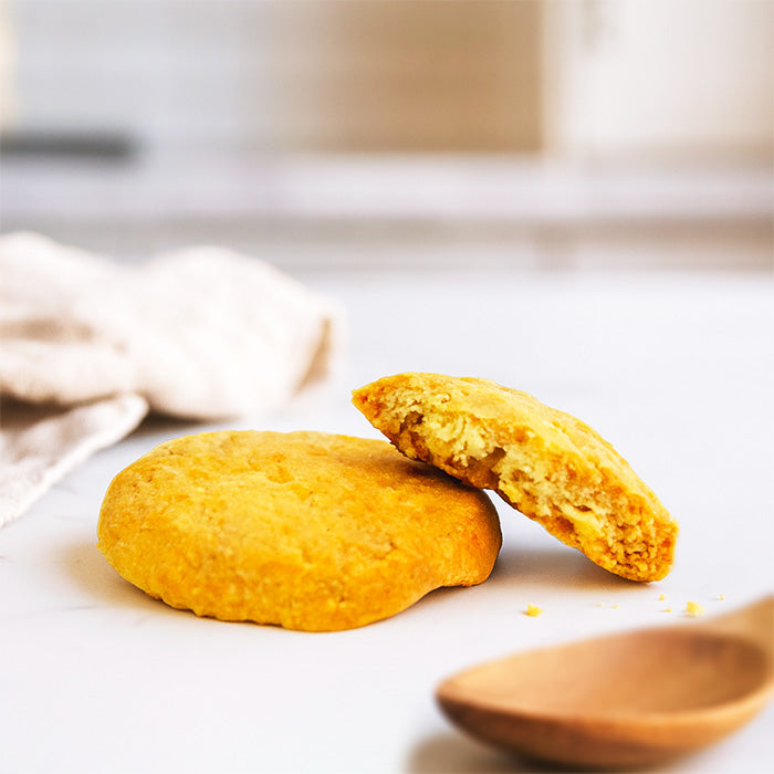 Sablé nature : deux biscuits dont un coupé, cuillère en bois au premier plan, serviette et table de cuisine en fond