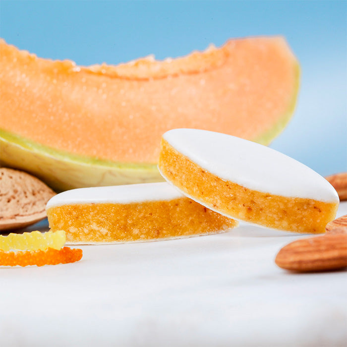 Calissons d'Aix artisanaux avec écorces d'oranges, amandes et tranche de melon en arrière-plan
