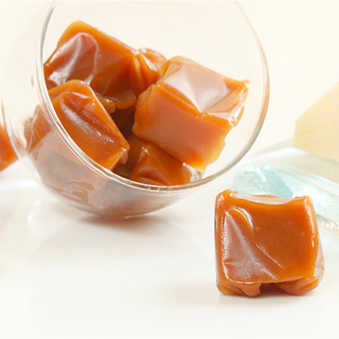Caramels au beurre salé dans une coupelle en verre avec un caramel devant et beurre breton en coin sur fond blanc