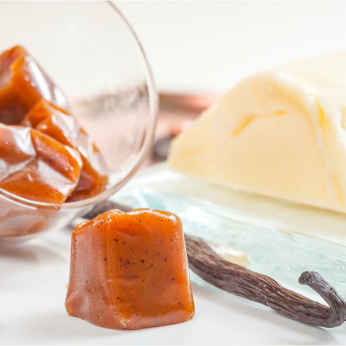 Caramels au beurre salé à la vanille dans une coupelle en verre avec beurre breton et gousse de vanille sur fond blanc