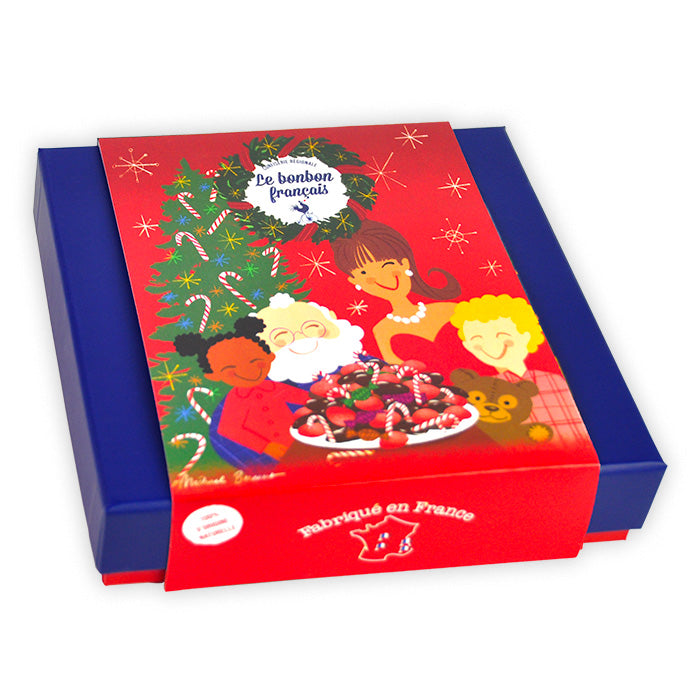Coffret prestige Noël fermé dans son fourreau rouge illustré d'une scène familiale autour d'une table de bonbons avec sapin de Noël