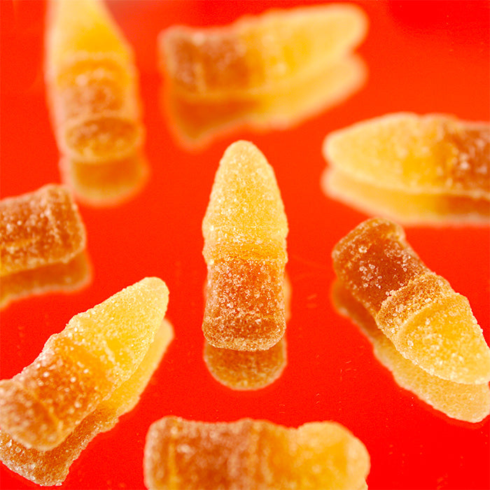 Cola des Coqs : huit bonbons en forme de bouteille de cola posés sur une table rouge