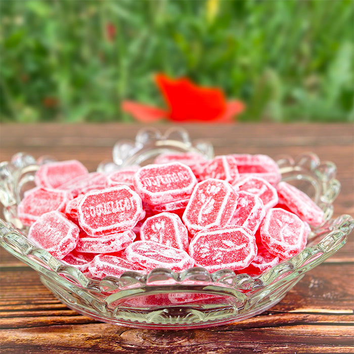 Coupelle en verre remplie de bonbons coquelicots sur table en bois avec champ de coquelicots en arrière-plan