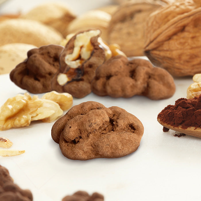 Croc Noix du Quercy en gros plan avec trois autres dont un coupé, cerneaux de noix et poudre de cacao sur cuillère en bois