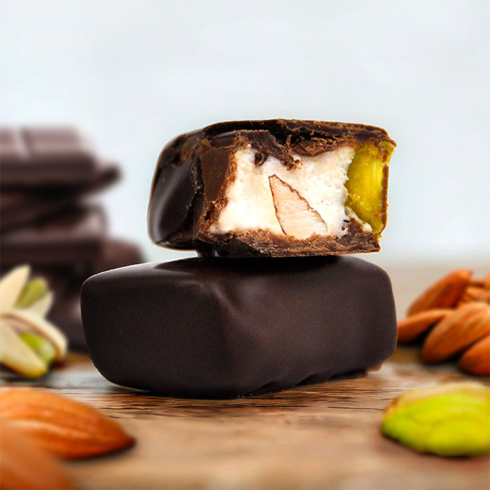 Tendre nougat enrobé de chocolat en gros plan, un coupé révélant l'intérieur, avec amandes, pistaches et éclats de chocolat