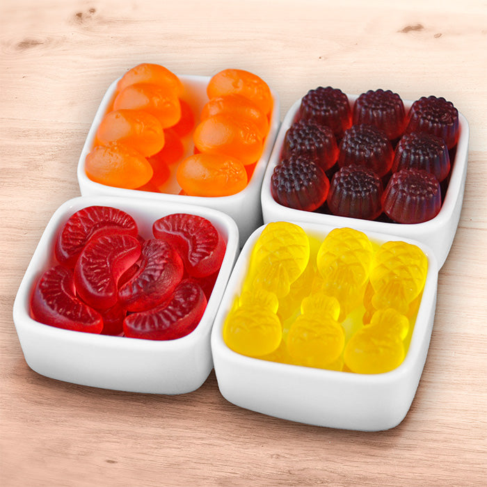Méli-Mélo fruité : bonbons mangue, framboise, ananas et quartier d'agrumes dans leurs coupelles blanches sur table en bois