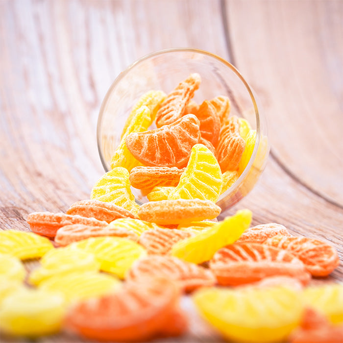 Pas d'Quartier : coupelle en verre renversée laissant s'échapper des bonbons en forme de quartiers jaunes et oranges sur table en bois