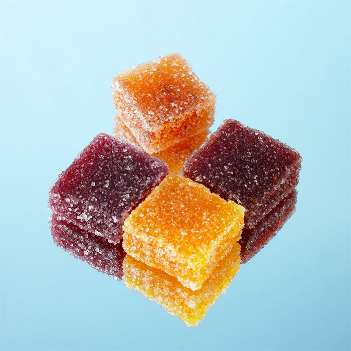 Pâtes de fruits artisanales : quatre pièces multicolores côte à côte sur miroir avec reflet, fond bleu
