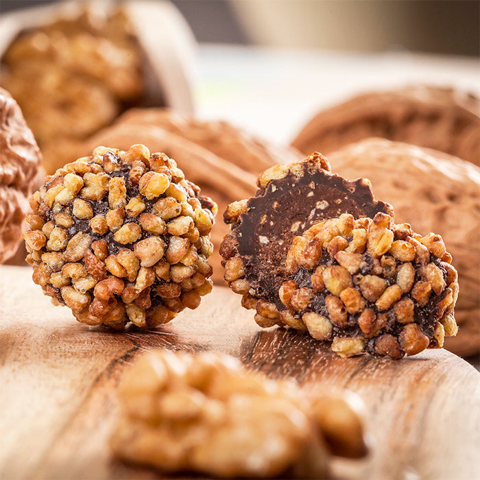 Sac de billes chocolatés artisanaux sur planche ronde en bois, cerneaux de noix floutés en arrière-plan sur fond blanc