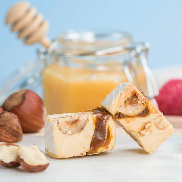 Tendre nougat au caramel beurre salé en gros plan avec noisettes, pot de miel en arrière-plan sur marbre et fond bleu