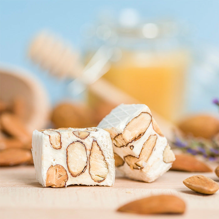 Nougat tendre de Provence aux amandes, recette artisanale de Montélimar, avec miel en arrière-plan